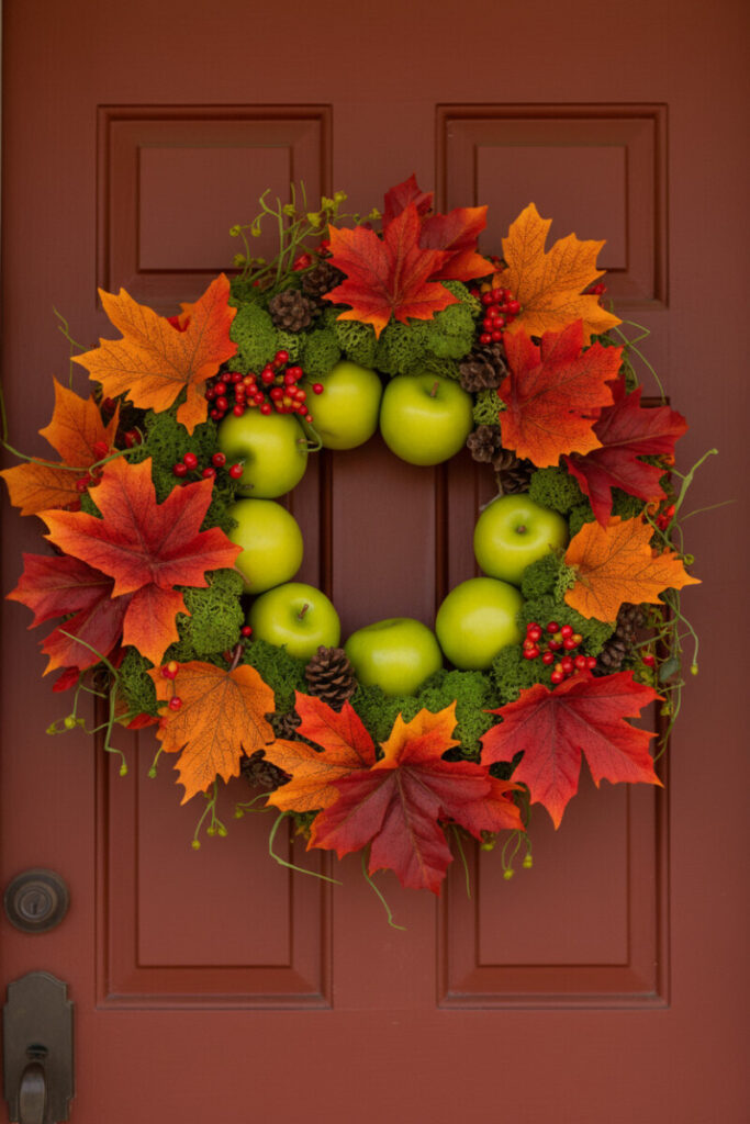 Nine bright green apples nestled among saturated crimson and orange maple leaves on a glossy brick-red paneled door.