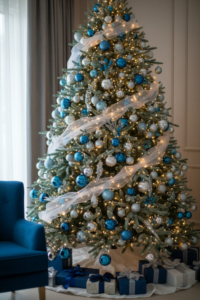 Gossamer white ribbon drifting through branches with deep sapphire and bright silver ornaments, white skirt and navy-silver gifts—polished modern holiday decorating touch.