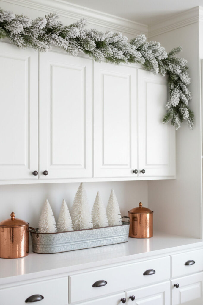 Flocked snowy garland on white uppers and a galvanized trough of fuzzy white trees with copper canisters.