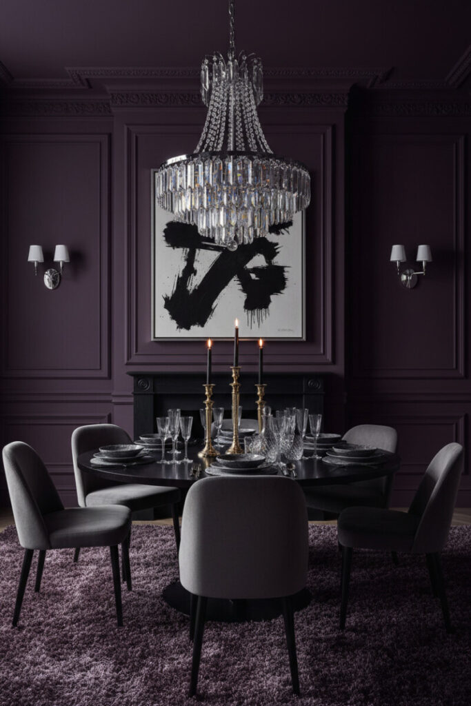 Aubergine walls, crystal chandelier, velvet chairs, and brass candelabras—Moody Dining Room Designs in a jewel-box palette.