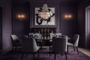 Aubergine walls, crystal chandelier, velvet chairs, and brass candelabras—Moody Dining Room Designs in a jewel-box palette.