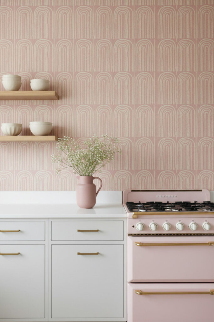Cream arch-pattern dusty pink wallpaper, off-white bases, and blush enamel range—smart solution for how to style a pink kitchen.