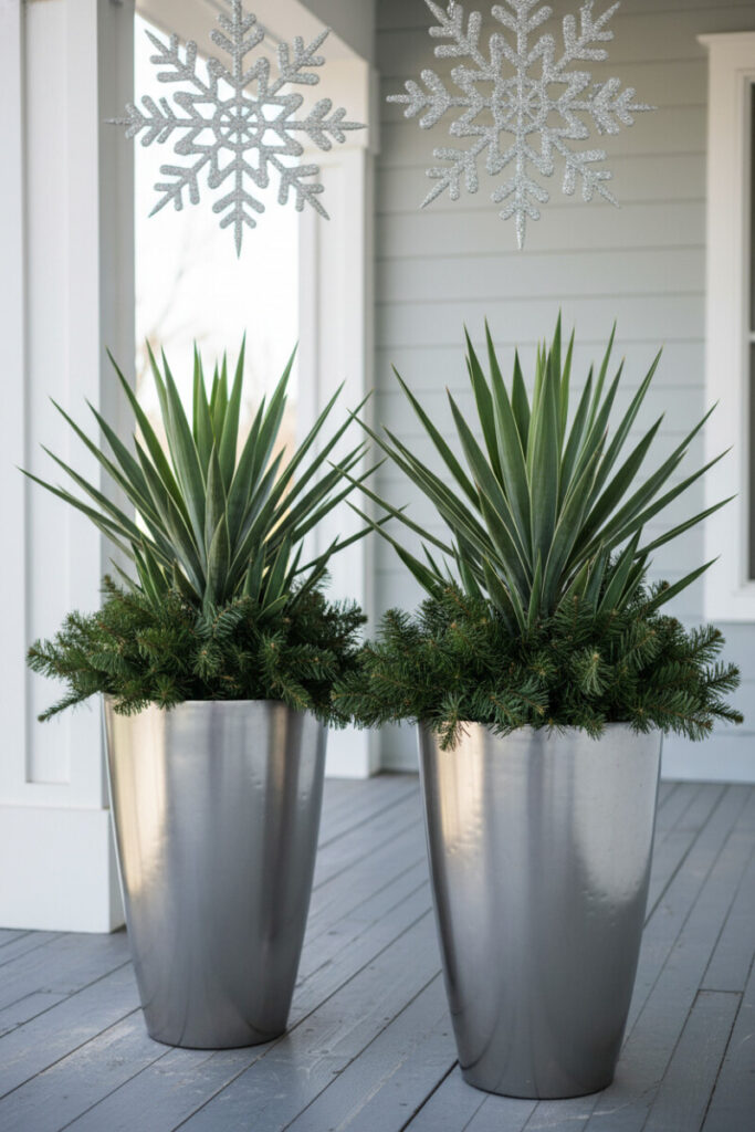 Brushed steel bullet planters with Snowflake Yucca under glitter snowflakes on indigo-gray deck—sleek small porch winter decorating ideas.